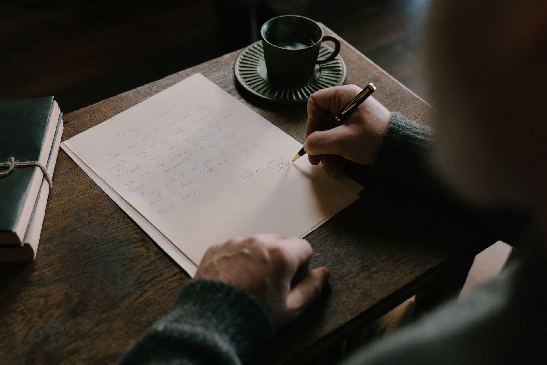 A person writing a letter at a wooden desk.