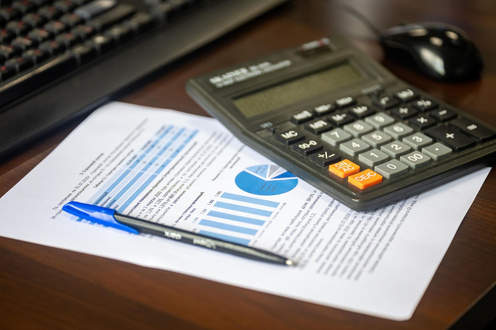 Desk with a calculator, financial report and pen, suggesting cost analysis.